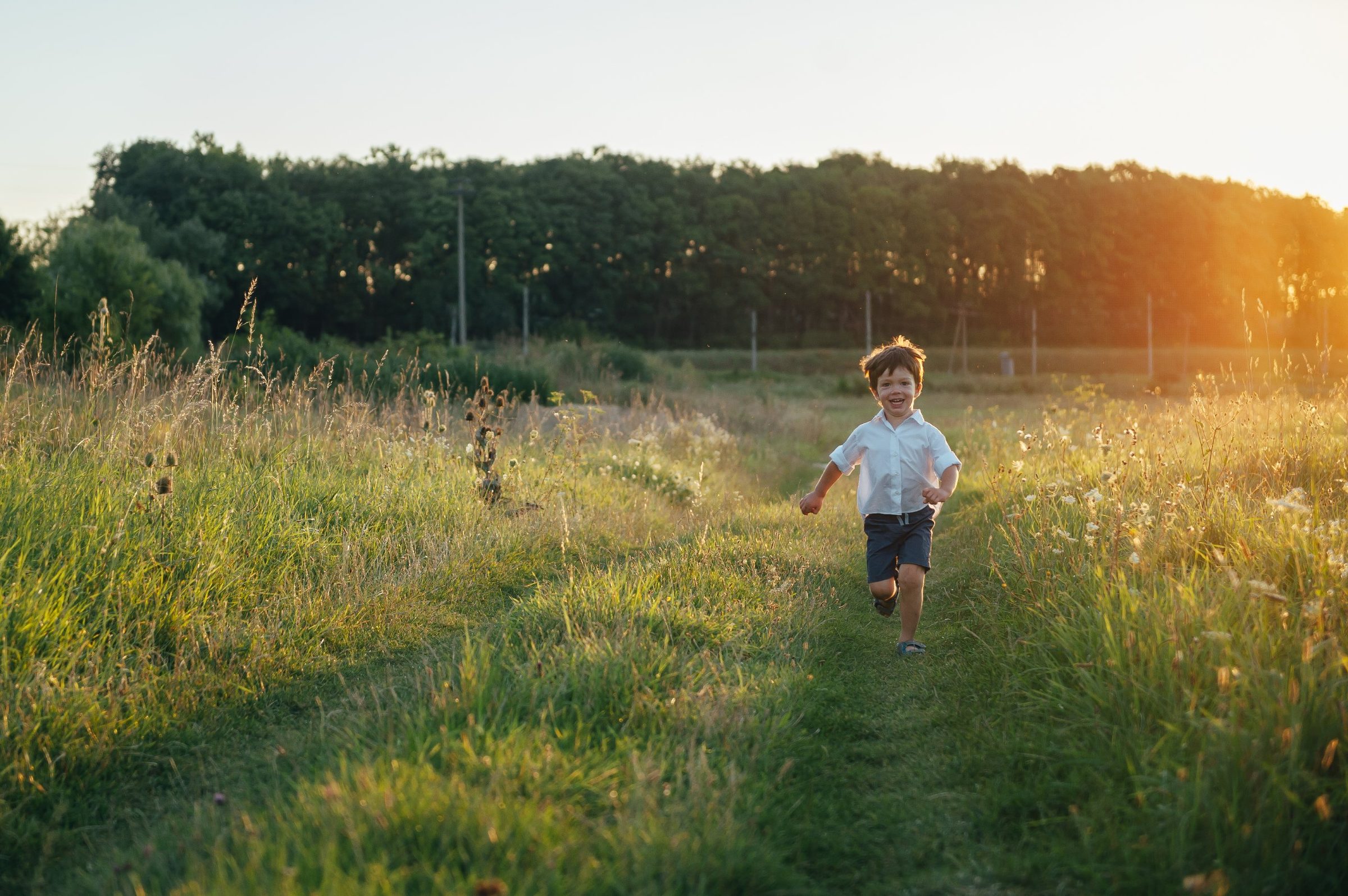 A young boy running along a grassy path through a meadow at sunset