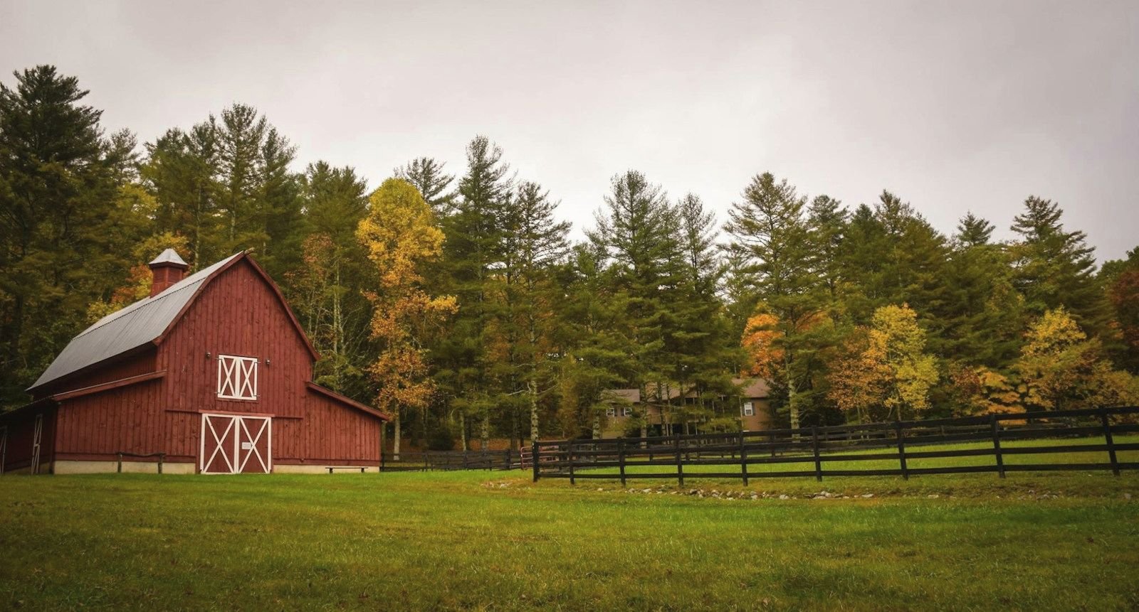 A red barn beside a green pasture and autumn trees