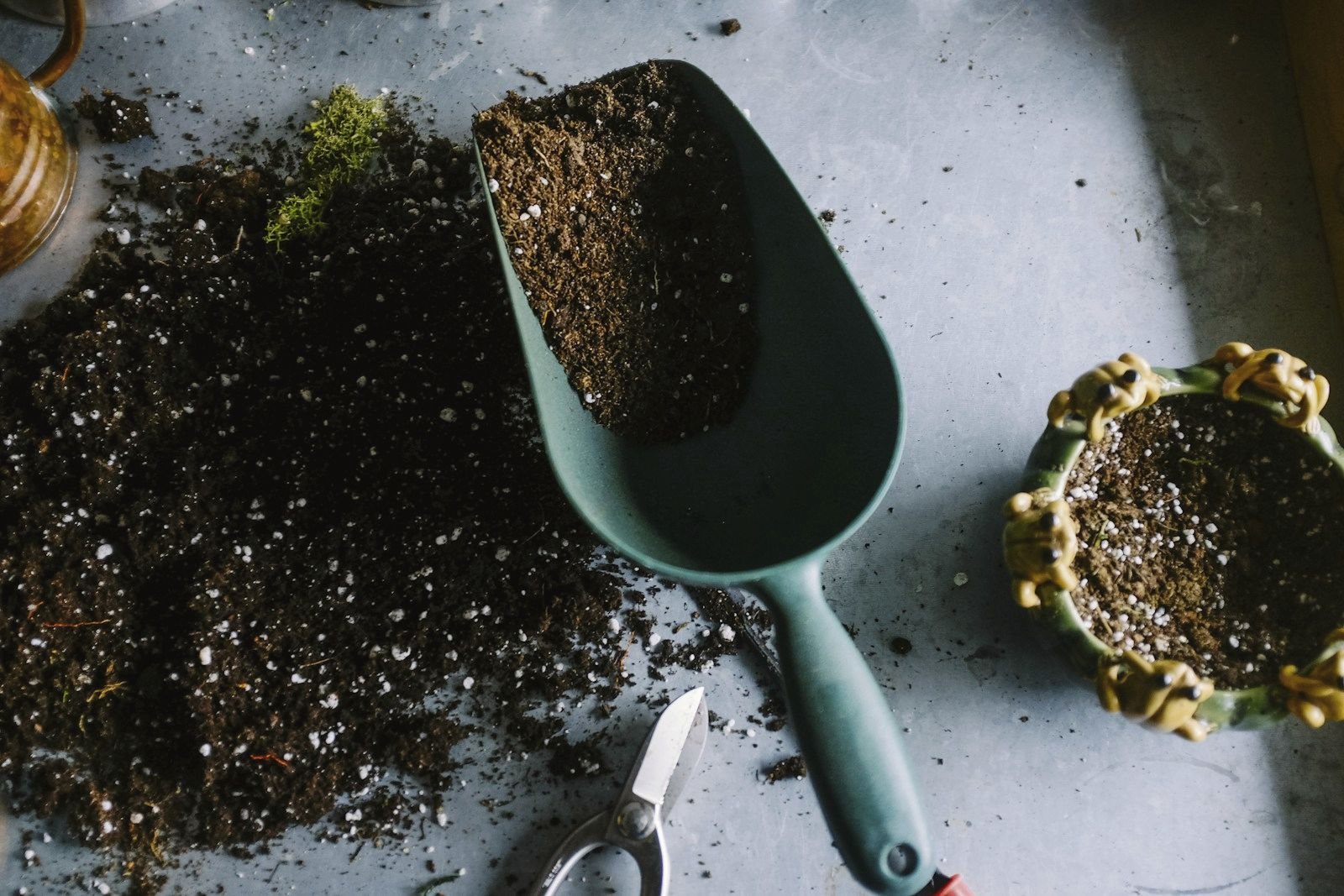 A garden trowel scooping dark soil beside a small pot